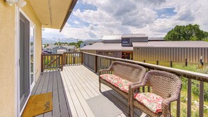Um deck de madeira com móveis de vime e vista para montanhas e um edifício ao fundo.