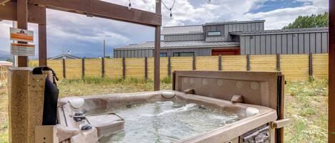 A hot tub with a stone exterior, wooden deck, and a view of a modern building in the background.