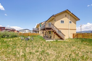 Et tosyltet hus med en trætrappe, der fører op til en balkon, omgivet af en indhegnet gårdhave med udendørs siddepladser.