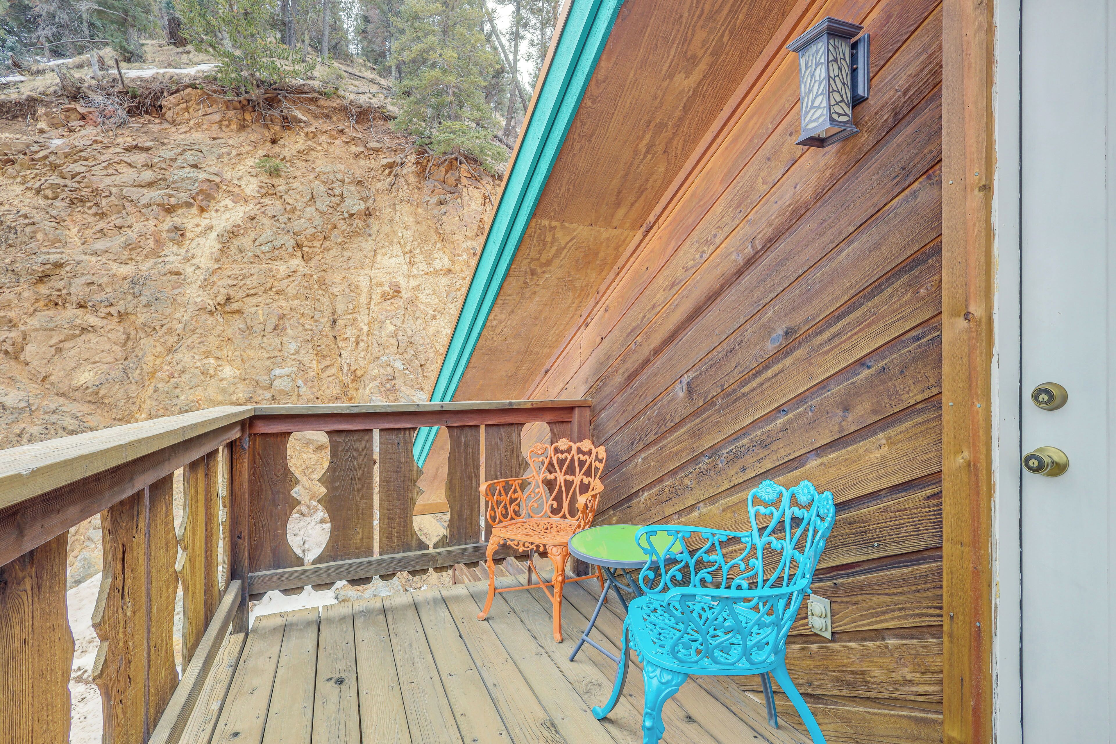 Une terrasse en bois avec deux chaises en métal et une petite table, donnant sur une colline rocheuse.