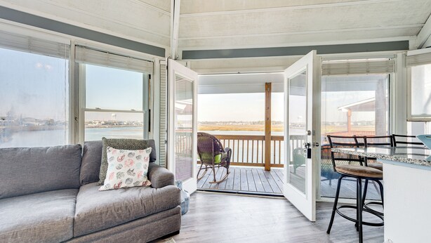 Un ampio balcone con vista su un corpo d'acqua, un divano grigio con cuscini decorati e un pontile in legno.