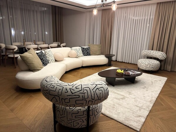 A modern living room with a curved sectional sofa, patterned armchairs, a coffee table, and a dining area with chairs and a table.