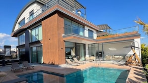 Une maison moderne à deux étages, dotée d’une piscine, d’une terrasse en bois et d’un espace salon extérieur.