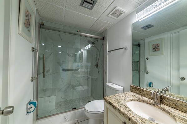 A modern bathroom with a glass-enclosed shower, a white toilet, and a granite countertop sink.