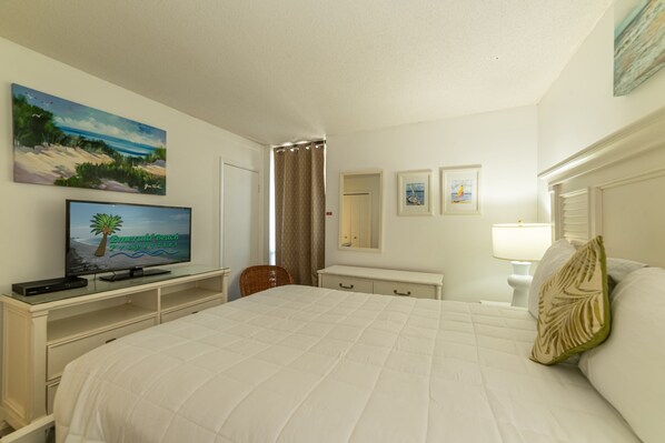 A hotel room with a large bed, a television on a stand, a desk with a chair, and a painting on the wall.