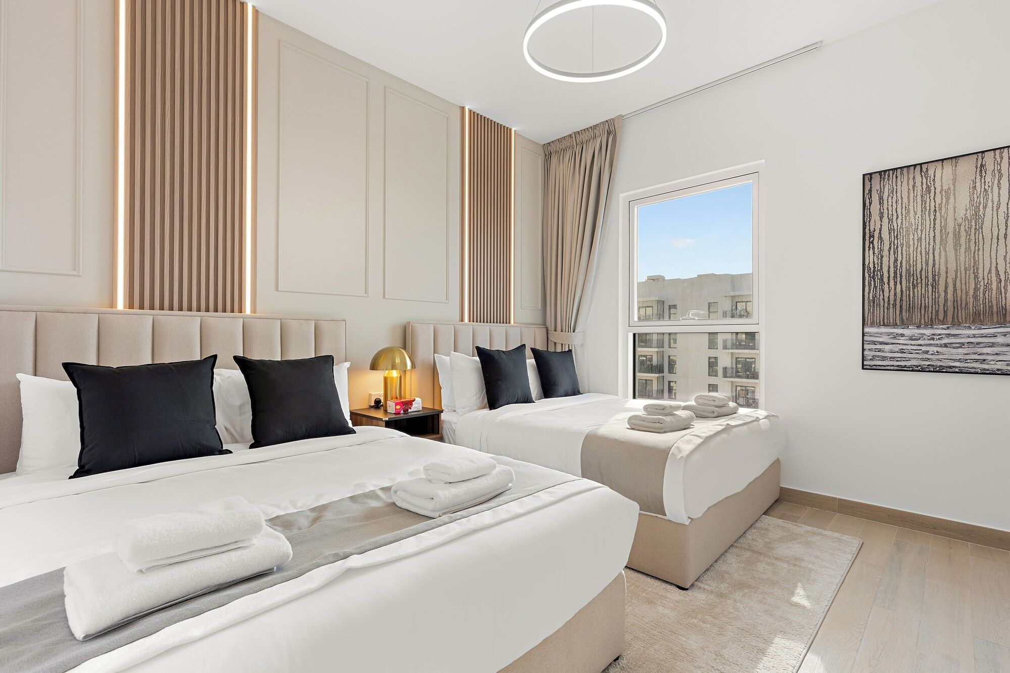 A hotel room with two beds, a large window, and a painting on the wall.