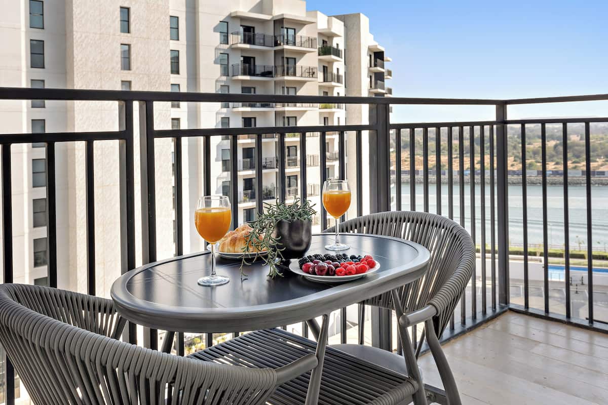 A balcony with a table set for two, featuring a plate of berries, a croissant, and two glasses of orange juice.