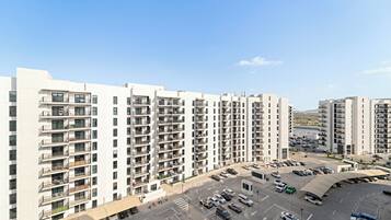 A high-rise residential building with multiple balconies, a parking area, and a clear view of the surrounding area.