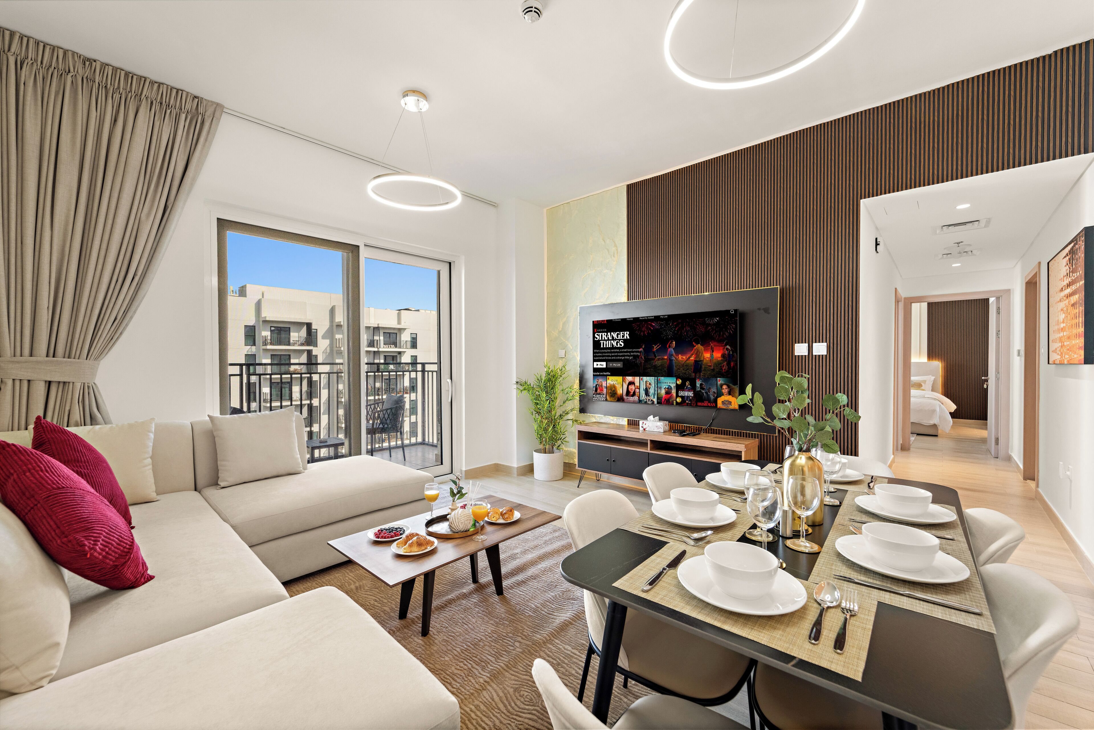 A modern living room with a sofa, dining table set for a meal, a television, and a balcony with a city view.