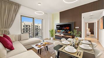 A modern living room with a sofa, dining table set for a meal, a television, and a balcony with a city view.