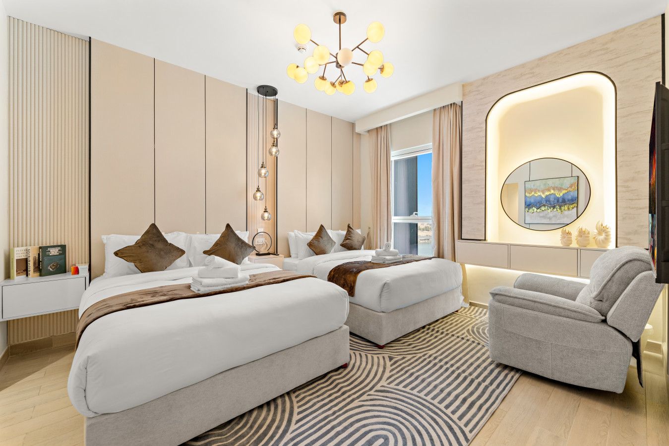 Quarto de hotel moderno com duas camas, área de estar, janela ampla e luminária de parede diferenciada.