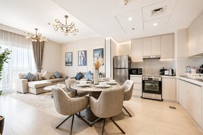 Una cocina moderna con electrodomésticos de acero inoxidable, una zona de comedor con una mesa y sillas redondas, y una sala de estar con un sofá y cojines decorativos.