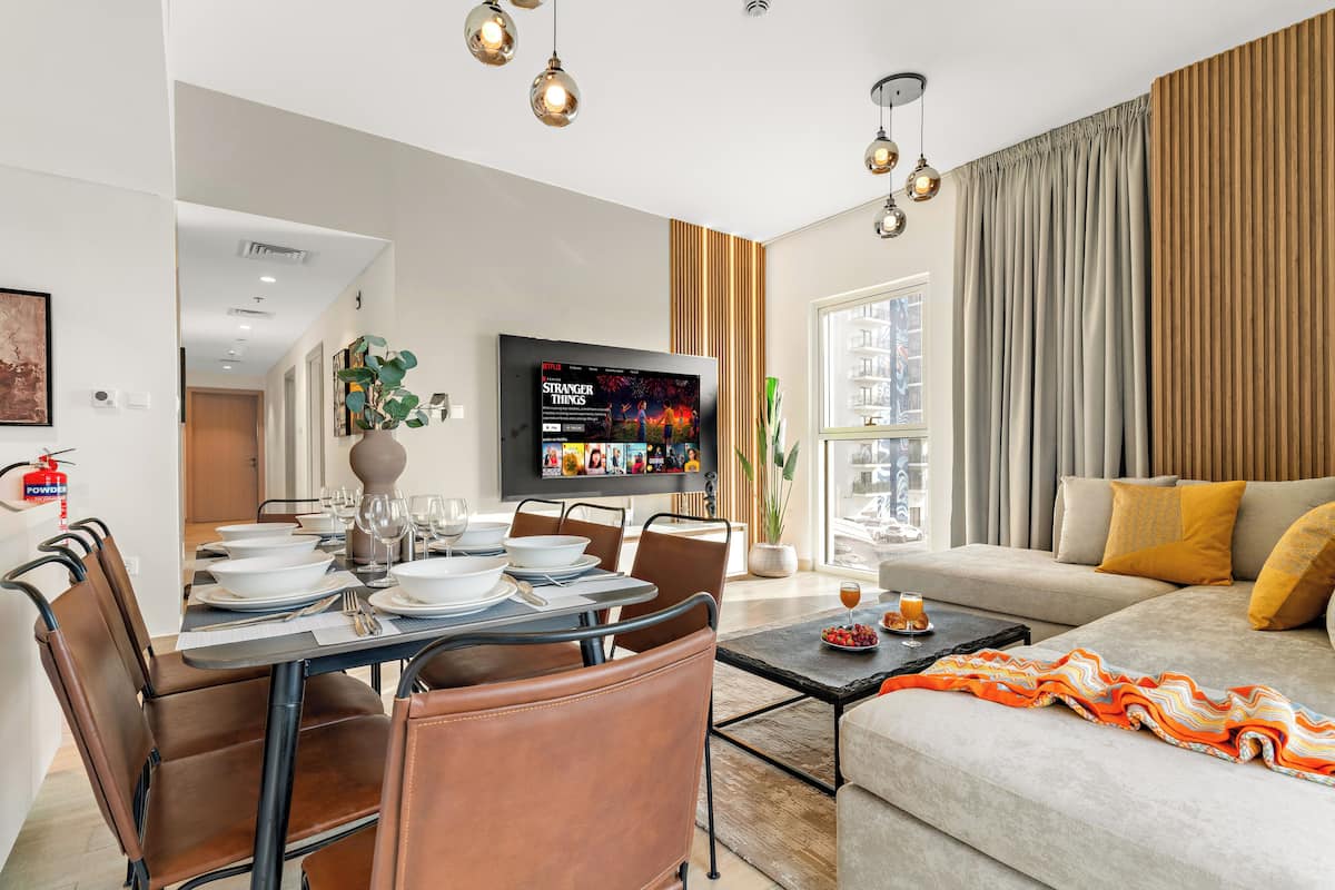 A modern living room with a dining area, a flat-screen TV, and a sofa with cushions.
