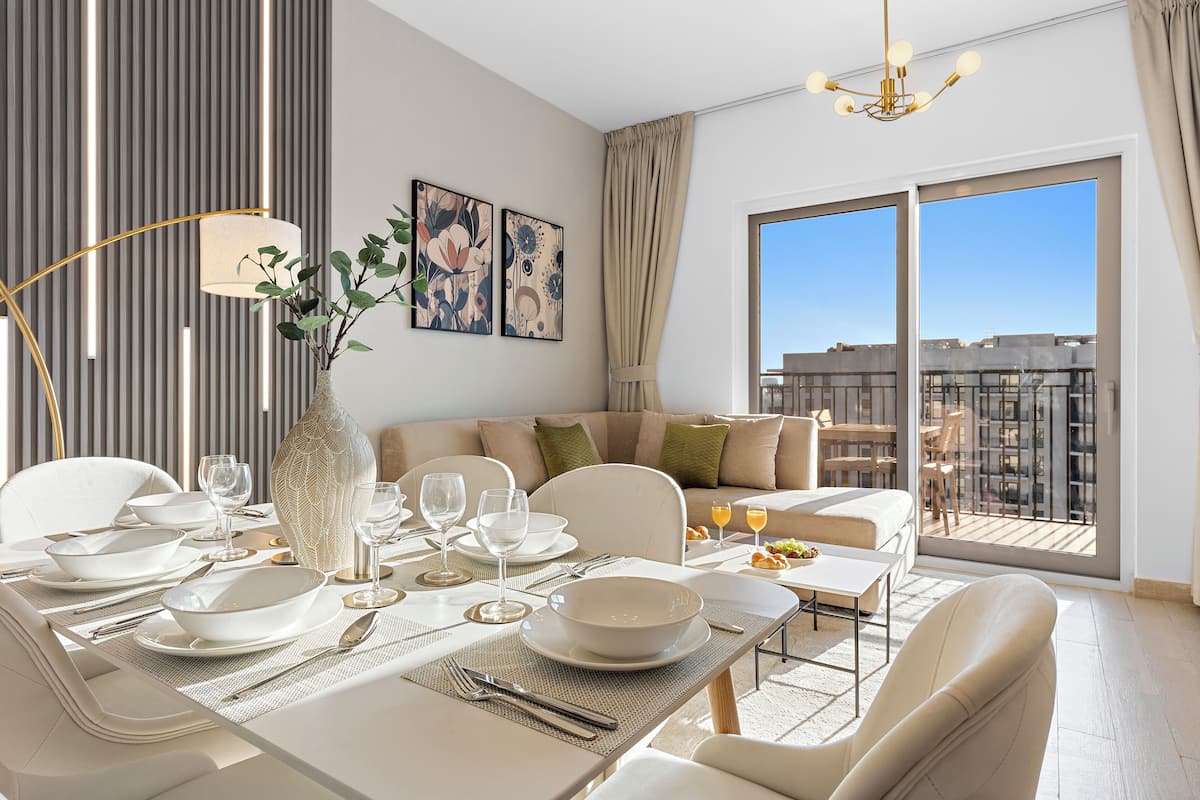 A modern dining area with a table set for four, a vase with greenery, and a city view through large windows.