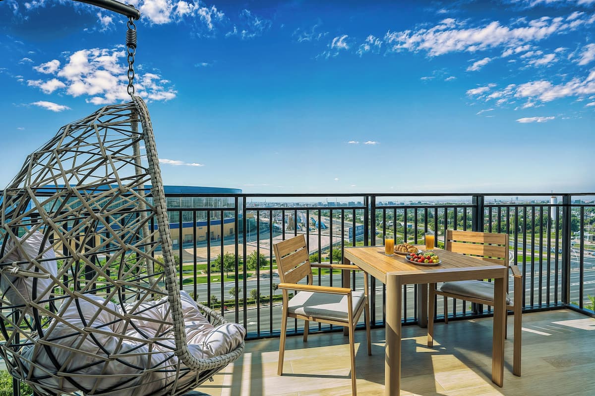 A balcony with a wicker chair, a wooden table, and a view of a cityscape.