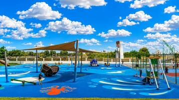 A playground with various play structures, a blue play area, and a clear sky with clouds.