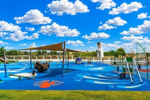 Un parque infantil con diversas estructuras de juego, una zona azul para jugar y un cielo despejado con nubes.