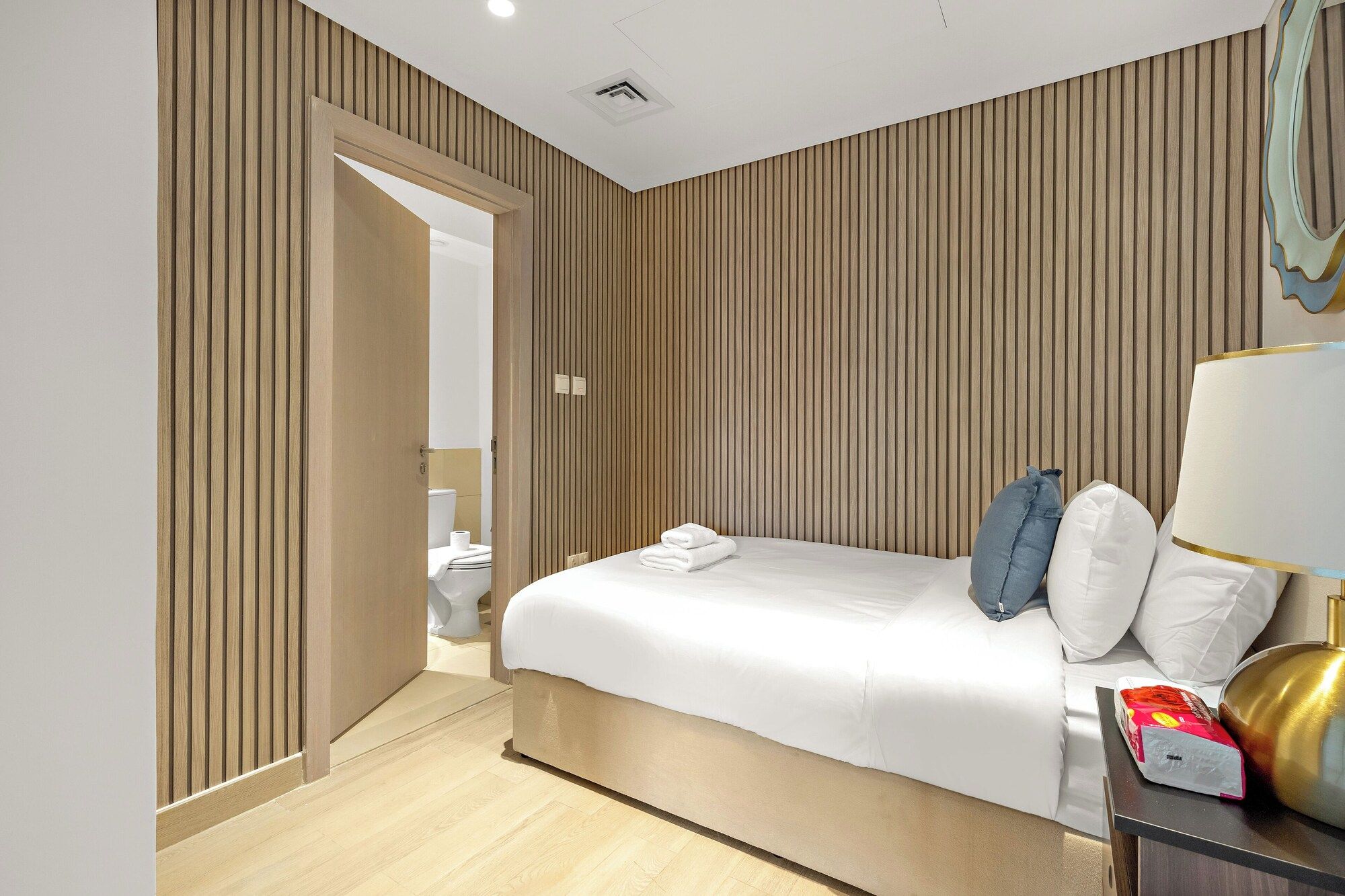 Ein Hotelzimmer mit Bett, Nachttisch, Lampe und Blick auf ein Badezimmer.