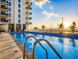 Una piscina con borde de azulejos, una escalera metálica y un edificio con balcones al fondo.
