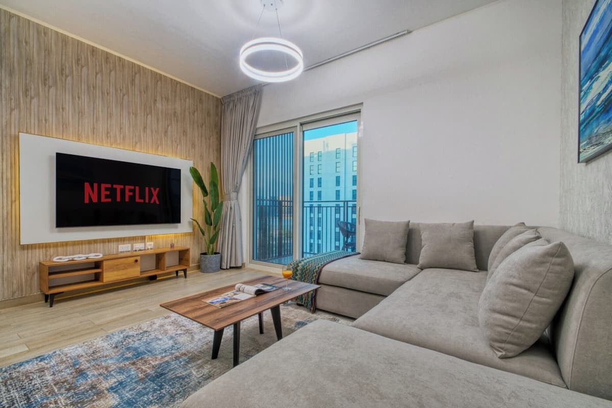 A modern living room with a large flat-screen TV mounted on the wall, a sofa, a coffee table, and a potted plant.