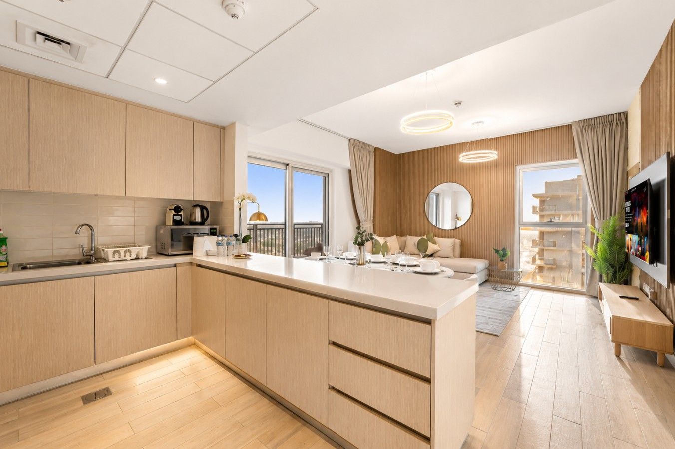 A modern kitchen with a central island, a dining area with a sofa, and a TV mounted on the wall.
