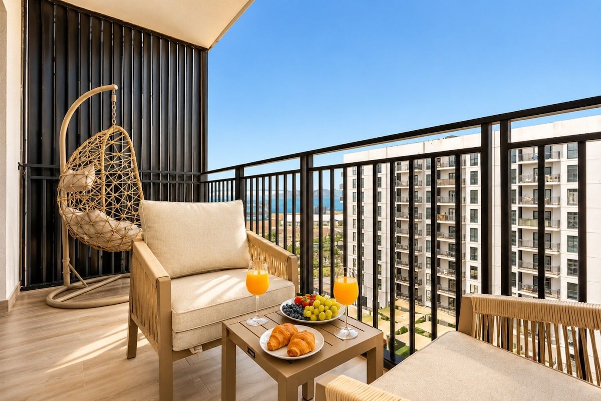 Un balcón con una silla de mimbre, una mesa con desayuno y vistas a un edificio alto.