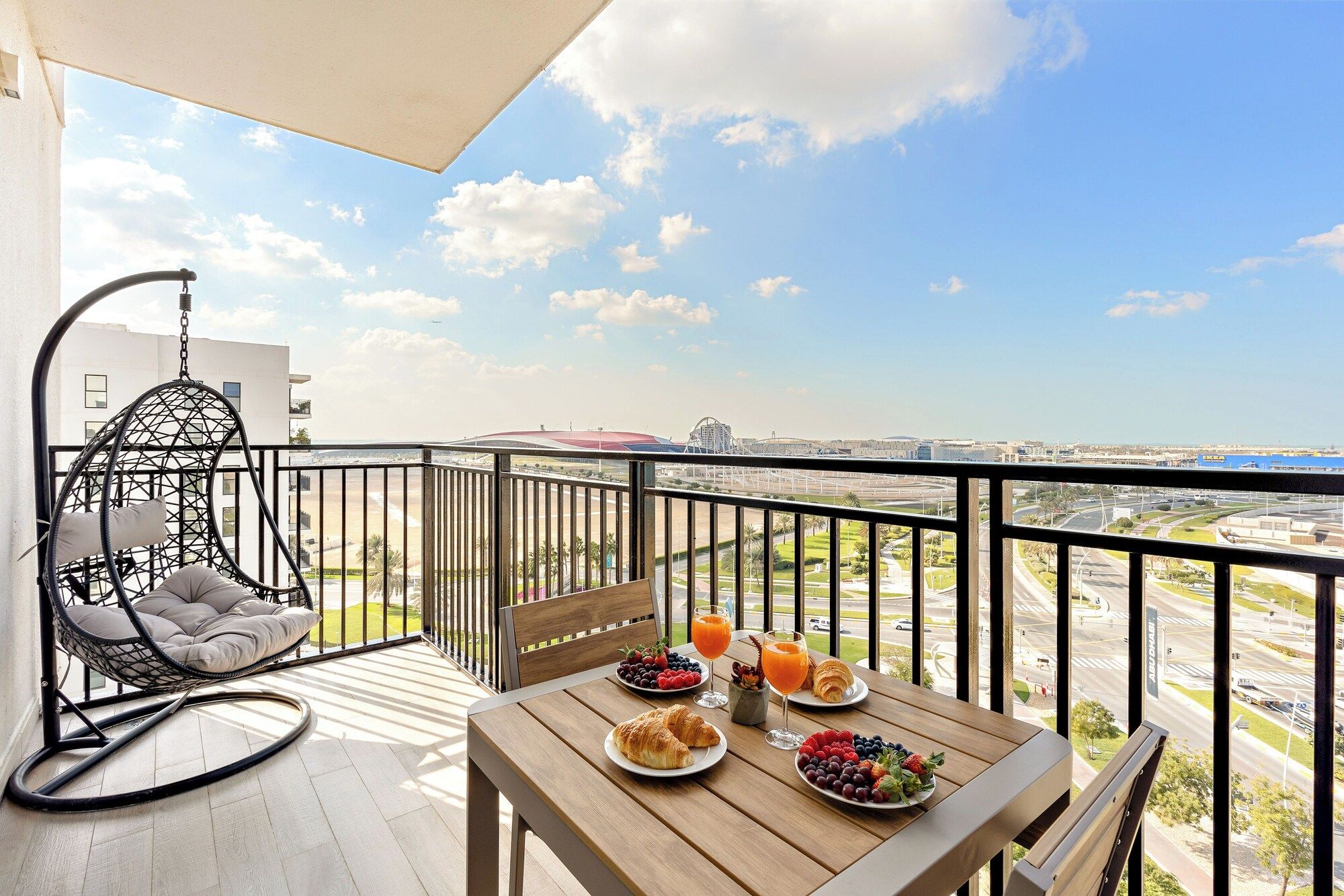 Ein Balkon mit einer Hängematte, einem Frühstückstisch und Blick auf eine Stadtlandschaft.