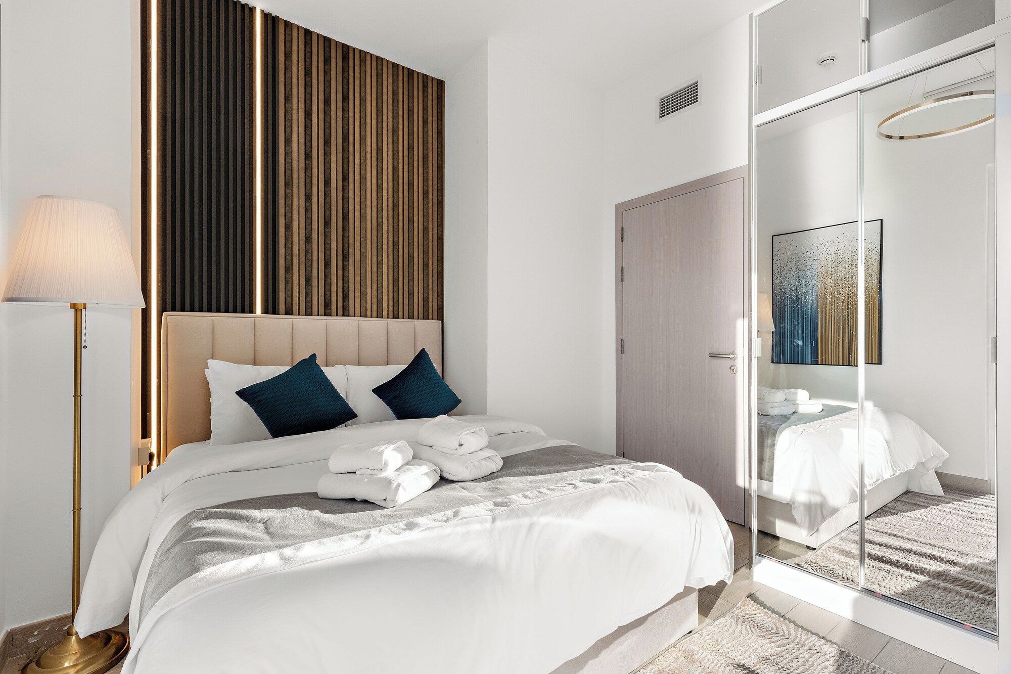 Habitación de hotel con una cama, lámpara de noche, armario y espejo que refleja la cama.