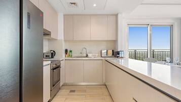 A modern kitchen with stainless steel appliances, light wood cabinetry, and a large window offering a view of the outdoors.