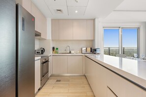 A modern kitchen with stainless steel appliances, light wood cabinetry, and a large window offering a view of the outdoors. - Desert Key - Perfectly Located Yas Island Premier Apts (Abu Dhabi)