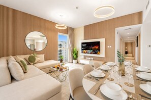 Una sala de estar moderna con un sofá, una mesa de comedor preparada para cuatro personas, un televisor de pantalla plana y un gran ventanal.