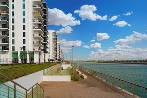 A waterfront promenade with a modern apartment building, a paved walkway, and a railing along the water.