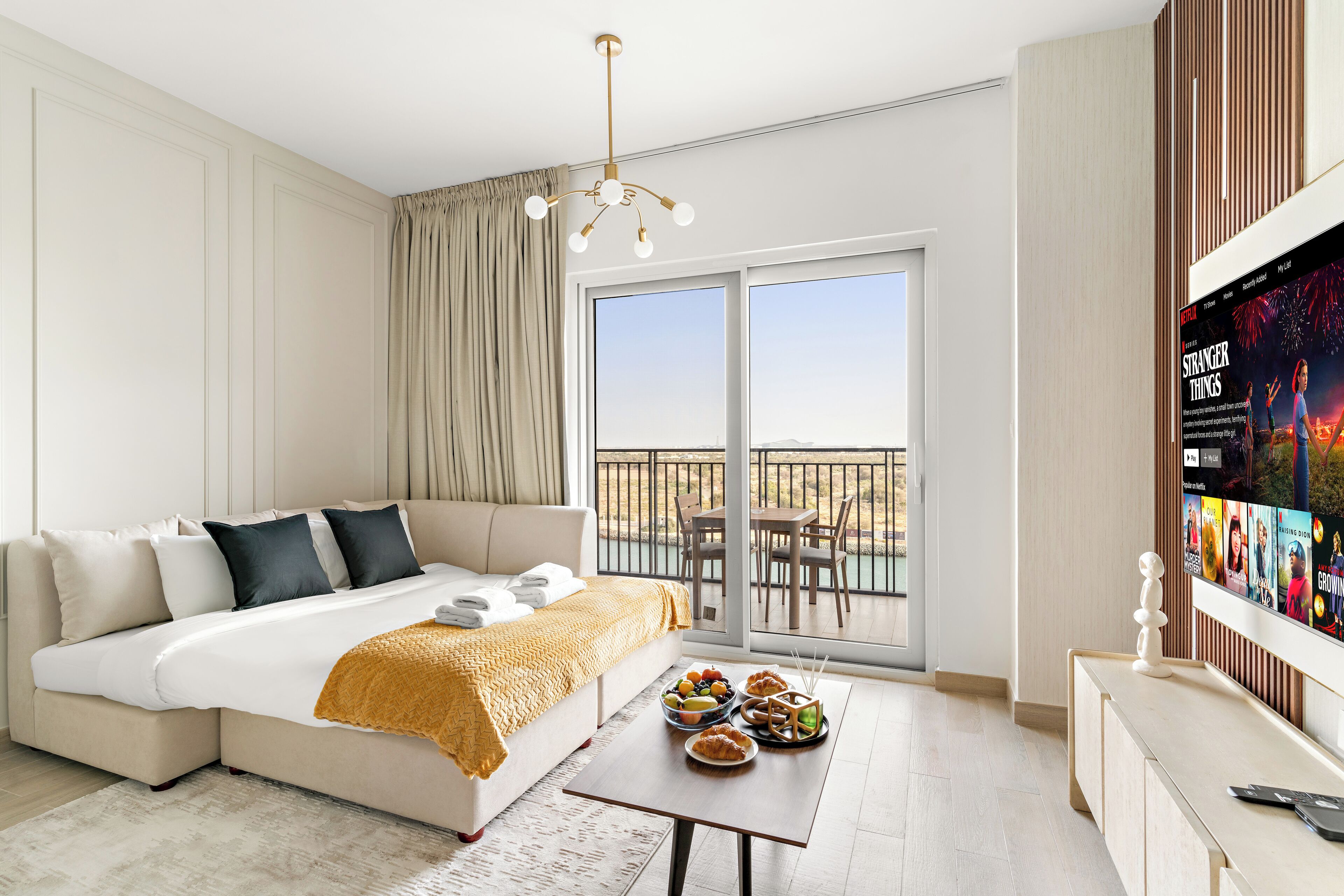 A modern hotel room with a large bed, a balcony with a view, and a television displaying a movie.