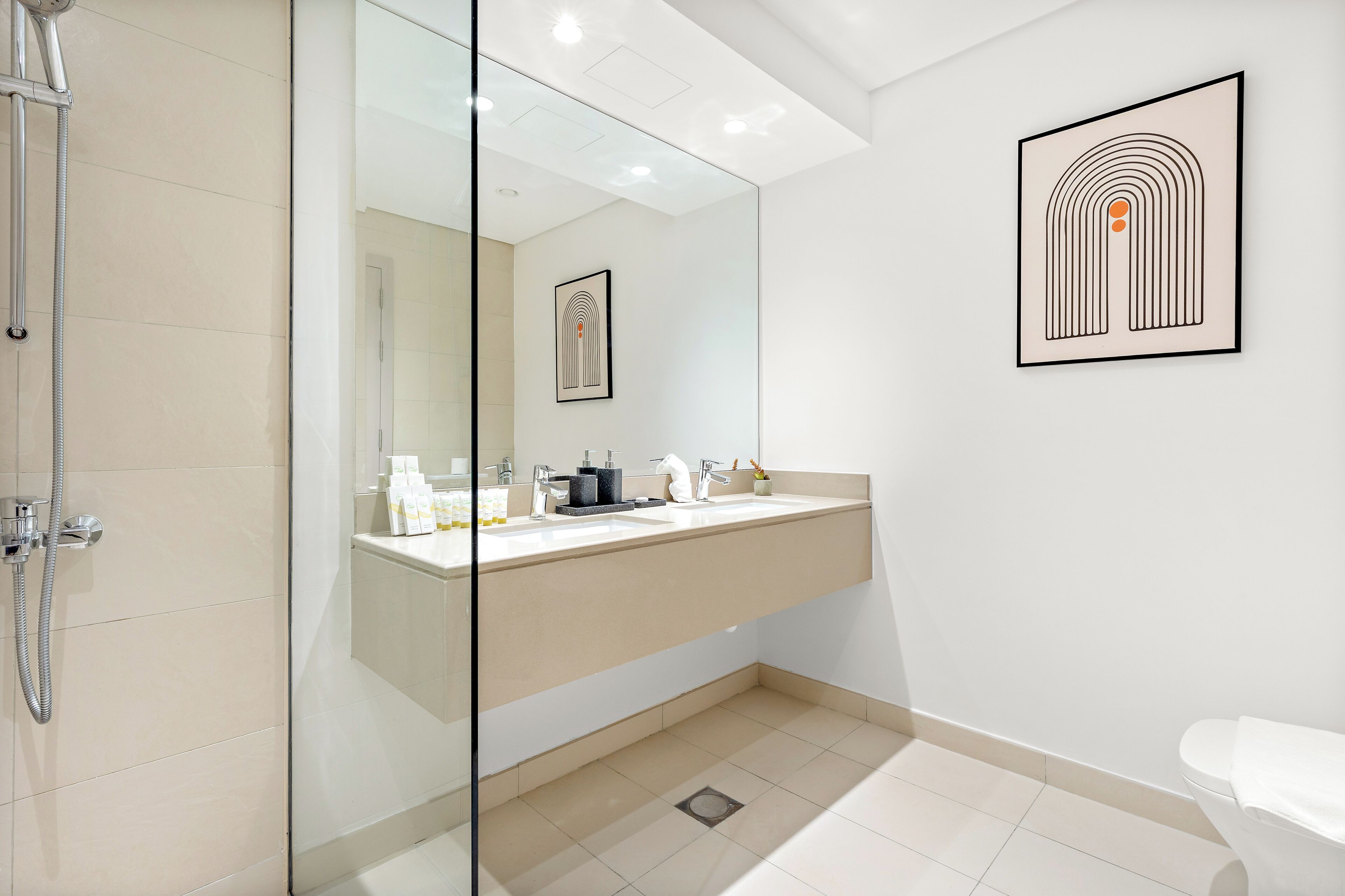 Un bany modern amb plat de dutxa de vidre, un lavabo doble i un vàter.