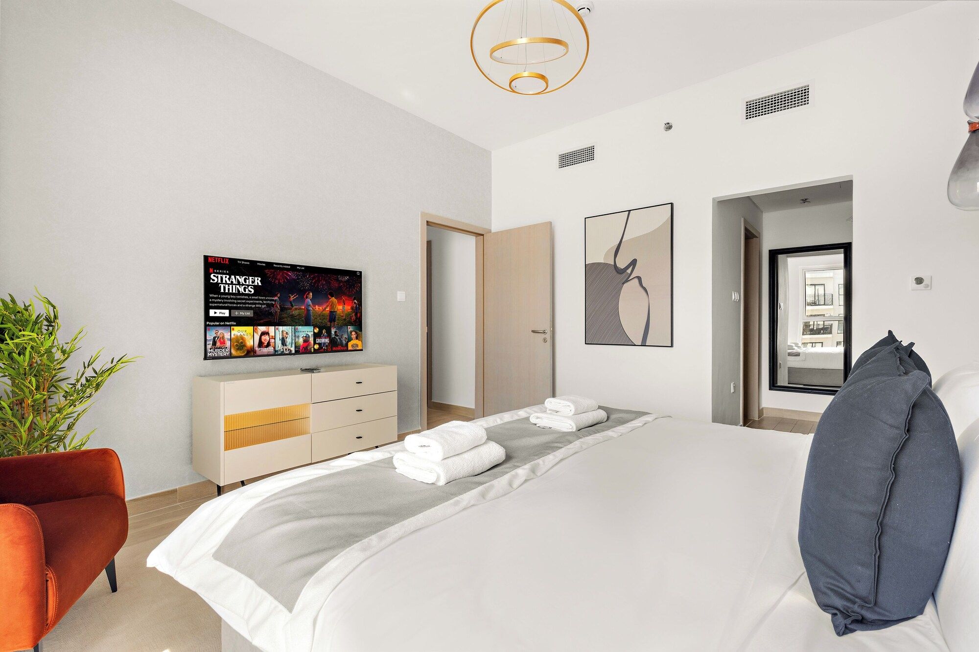 Ett modernt hotellrum med en säng, en tv som är monterad på väggen, en byrå och en krukväxt.