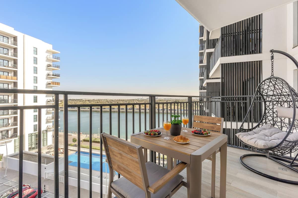 A balcony with a table set for two, a hanging chair, and a view of a body of water.