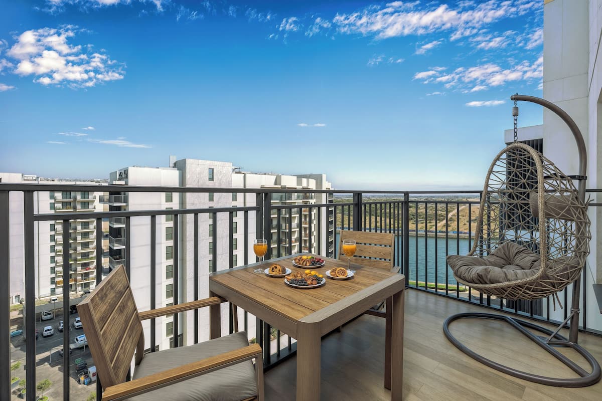 A balcony with a table set for breakfast, a hanging chair, and a view of the cityscape and water.