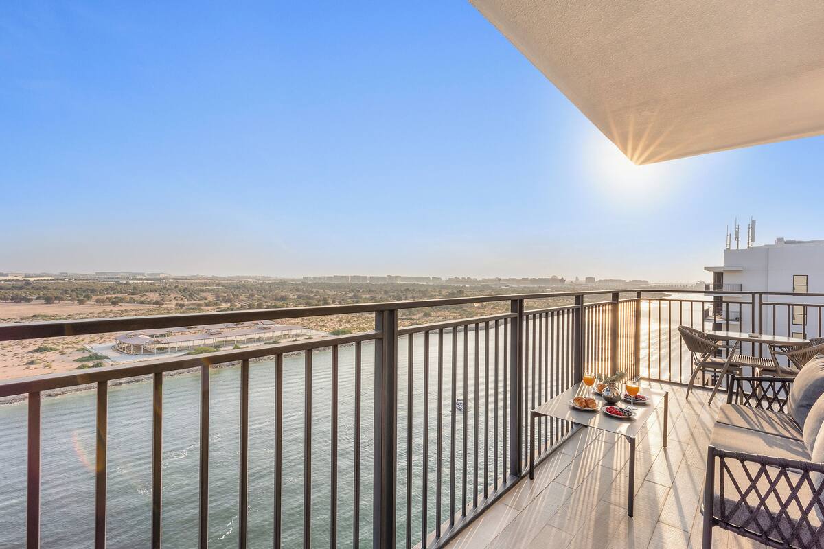 A balcony with a view of a river, a table with breakfast, and outdoor furniture.