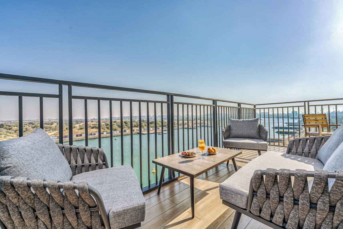 A balcony with a table, chairs, and a view of a body of water and distant landscape.