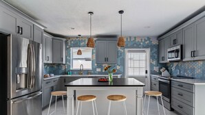 A modern kitchen with grey cabinets, stainless steel appliances, a central island with stools, and a decorative backsplash.