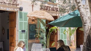 An outdoor cafe with wooden shutters, a thatched umbrella, and potted plants. - Hotelet Ca'n Oms Mozart by Rentallorca (Petra)