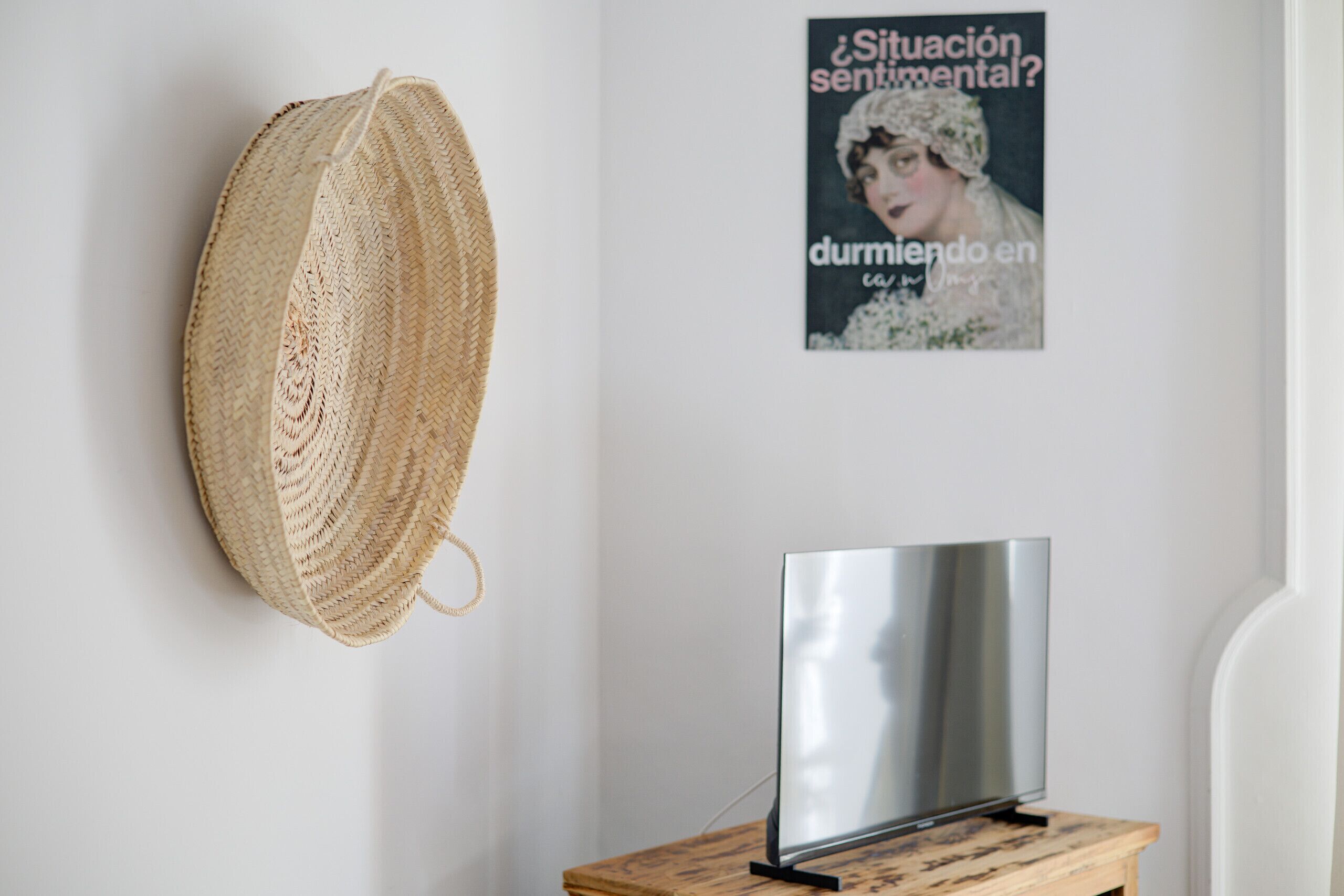 Un chapeau de paille accroché au mur, une affiche encadrée et un téléviseur à écran plat posé sur un meuble en bois.