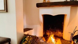 A fireplace with logs burning, a basket of firewood, and a metal container on the mantel. - Hidden gem Al Lago, authentic yet modern 2-bedroom house in medieval hamlet (Colonno)
