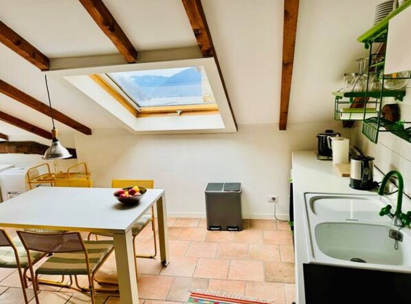 A compact kitchen with a skylight, a dining area with chairs, a trash bin, and a sink with a green faucet. - Hidden gem Al Lago, authentic yet modern 2-bedroom house in medieval hamlet (Colonno)