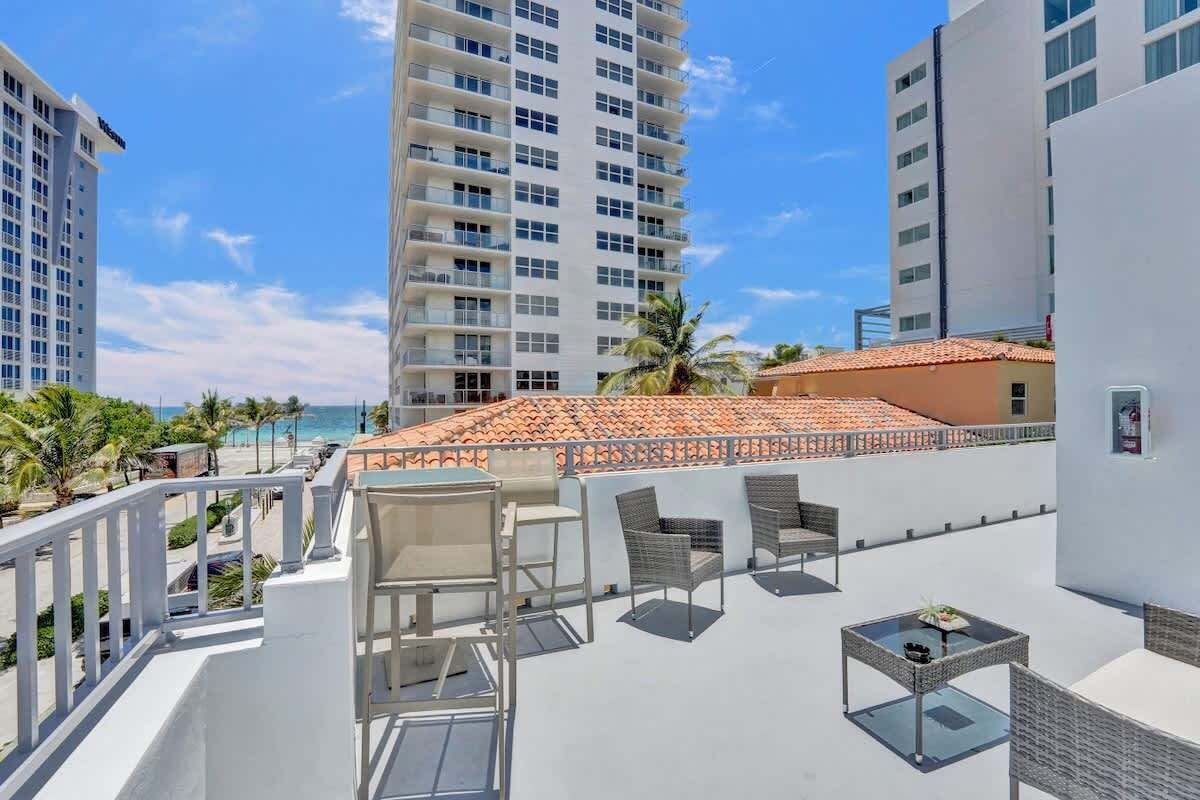 Une terrasse sur le toit, aménagée avec du mobilier d’extérieur, offrant une vue sur la plage et, en arrière-plan, sur les immeubles de grande hauteur.