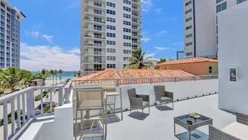Une terrasse sur le toit, aménagée avec du mobilier d’extérieur, offrant une vue sur la plage et, en arrière-plan, sur les immeubles de grande hauteur.