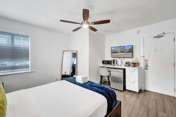 Habitación de hotel con cama, escritorio con microondas, silla, televisor y puerta.