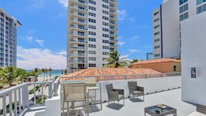 Une terrasse sur le toit, aménagée avec du mobilier d’extérieur, offrant une vue sur la plage et sur les grands immeubles qui se dressent à l’arrière-plan.