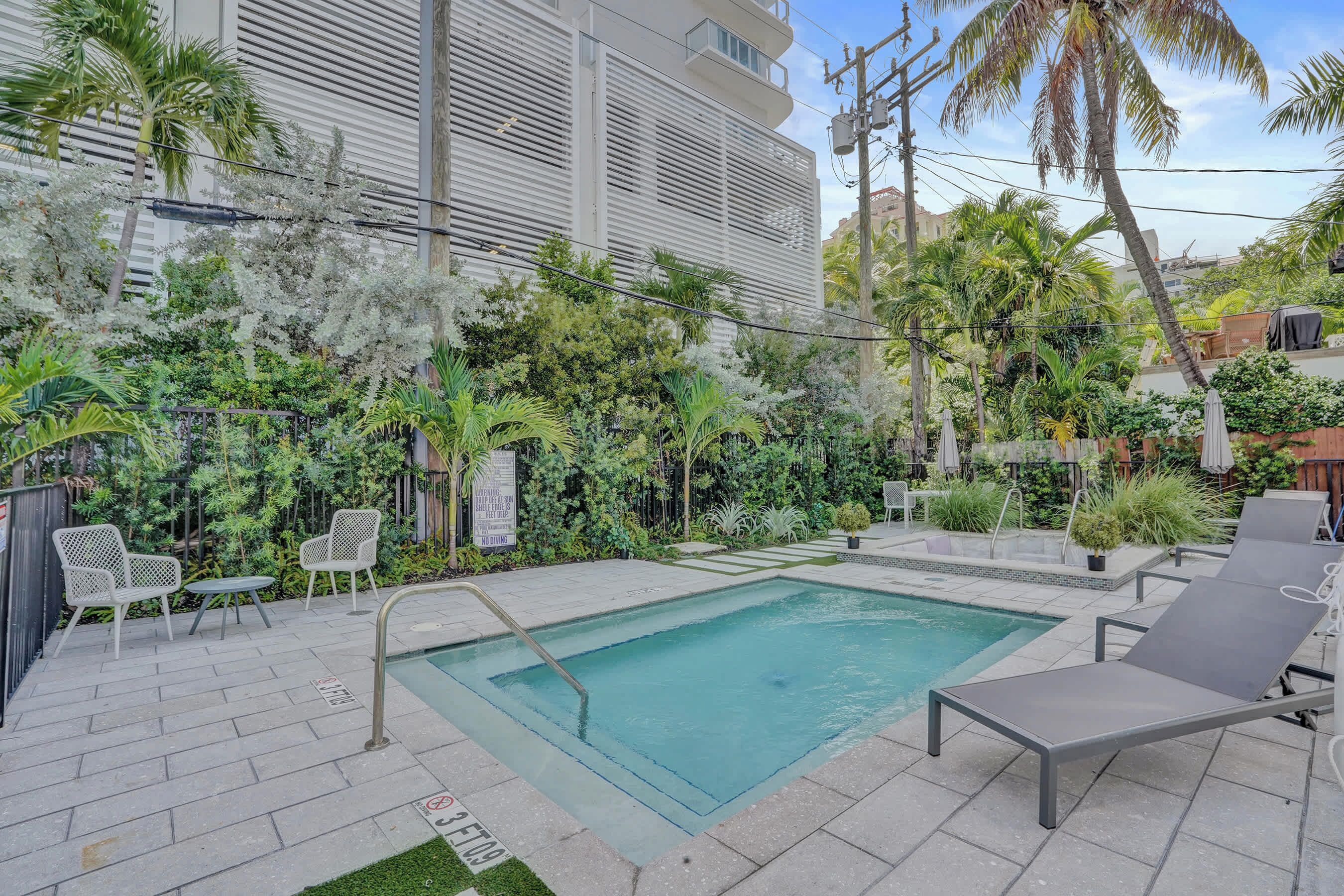 Una piscina con lettini, circondata da vegetazione lussureggiante e un edificio moderno.