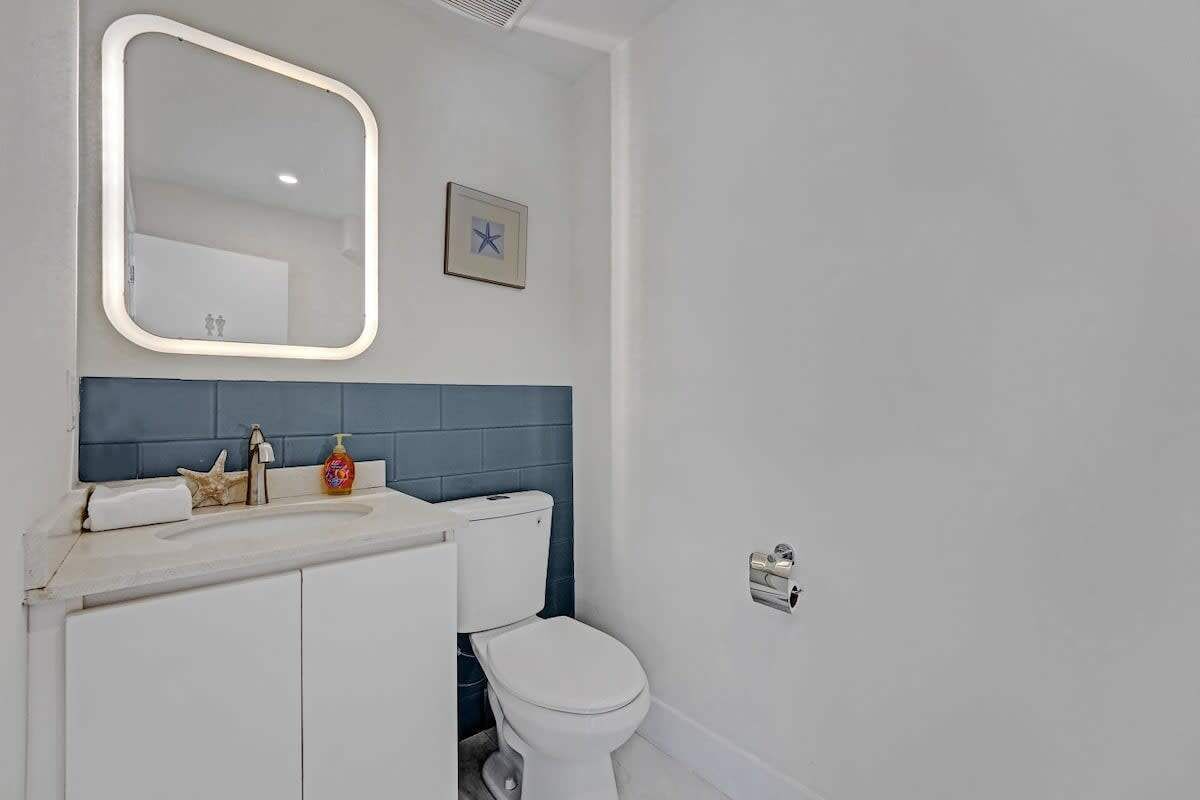 A bathroom with a white sink, a mirror, a toilet, and a blue-tiled wall.